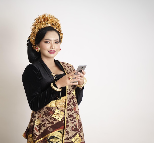 Sorridente donna balinese che indossa abiti tradizionali utilizzando smartphone