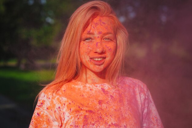 Sorridente donna bionda caucasica in posa con l'esplosione di vernice rosa al festival di Holi