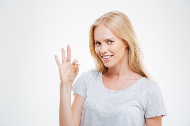 Sorridente donna bionda che mostra segno ok isolato su un muro bianco