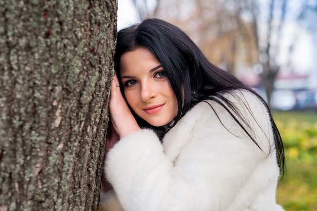 Sorridente donna bruna in posa vicino al tronco di un albero