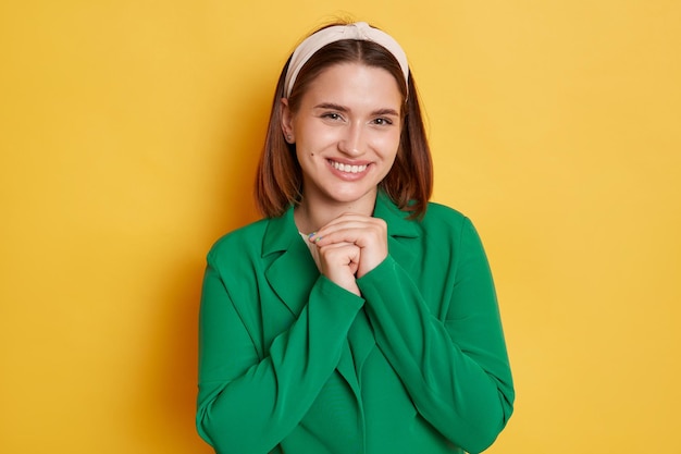 Sorridente donna carina che indossa una giacca verde in piedi isolata su sfondo giallo guardando la fotocamera con un sorriso felice che esprime emozioni positive