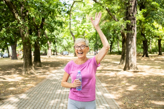 Sorridente donna caucasica anziana che saluta la sua amica mentre fa jogging nel parco.