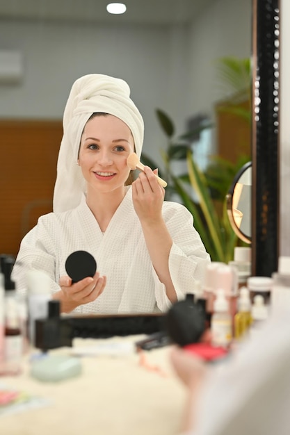 Sorridente donna caucasica che fa il trucco quotidiano e applica il pennello arrossisce in polvere sulle guance Cura di bellezza e concetto di cosmetici