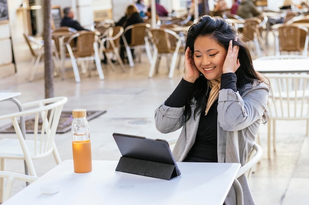 Sorridente donna d'affari asiatica in giacca e cravatta che lavora in remoto su tablet al telelavoro in terrazza all'aperto