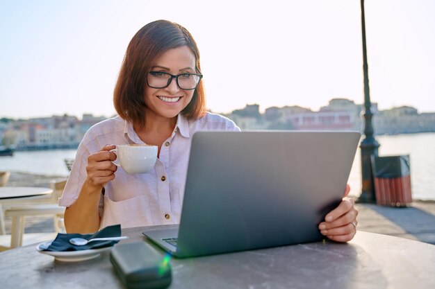 Sorridente donna d'affari di mezza età nella caffetteria con il computer portatile