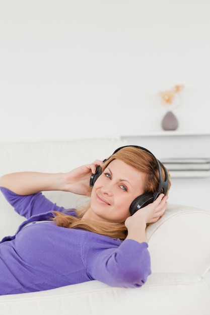 Sorridente donna dai capelli rossi, ascoltando musica e godendo il momento mentre sdraiata su un divano