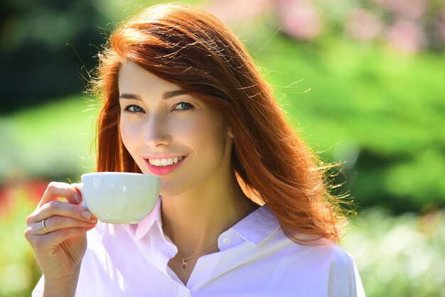 Sorridente donna dai capelli rossi tazza di caffè closeup ritratto di giovane bella donna che tiene la tazza di mor...