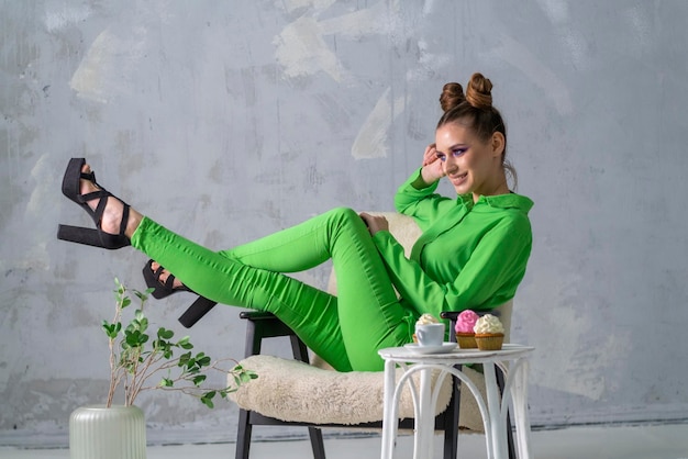 Sorridente donna elegante in abbigliamento verde seduto nella stanza luminosa Sfondo grigio