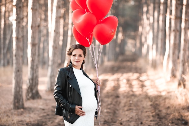 Sorridente donna incinta azienda palloncini a forma di cuore all'aperto Guardando la fotocamera Maternità Maternità