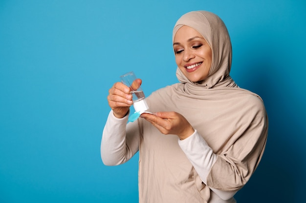 Sorridente donna musulmana che indossa l'hijab beige che applica la lozione per il trucco micellare al batuffolo di cotone.