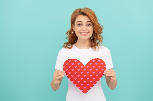 Sorridente donna rossa tenere cuore rosso su sfondo blu