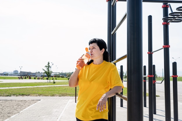 Sorridente donna senior di acqua potabile dopo l'allenamento all'aperto sul campo sportivo