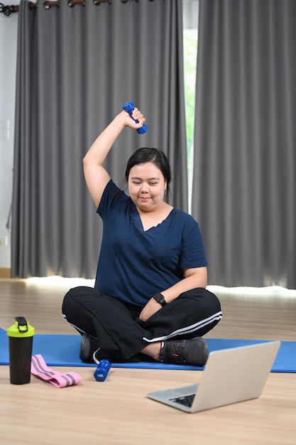 Sorridente donna sovrappeso che si esercita e guarda video di allenamento fitness online sul laptop a casa.