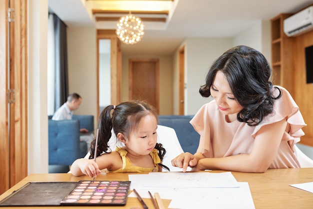 Sorridente donna vietnamita che punta a disegnare su sua figlia e chiedendole di disegnare più dettagli