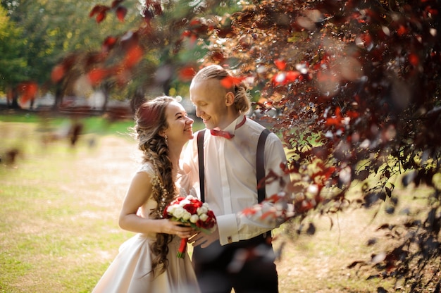 Sorridente e felice coppia sposata che cammina in un parco verde con prato e bellissimi alberi