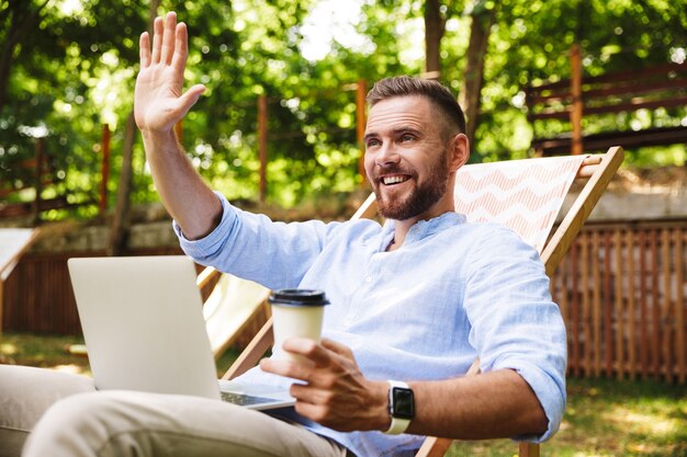 Sorridente emotivo giovane uomo barbuto sventolando tenendo il caffè.