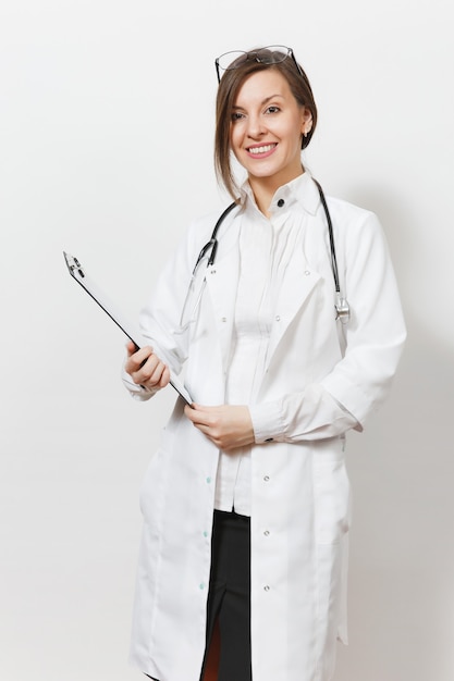 Sorridente fiducioso giovane medico donna con stetoscopio, occhiali isolati su sfondo bianco. Medico femminile in abito medico che tiene la tessera sanitaria sulla cartella del blocco note. Concetto di medicina del personale sanitario.