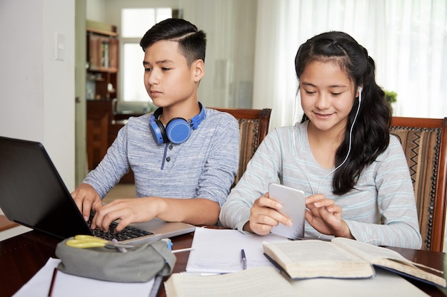 Sorridente fratello e sorella adolescenti che fanno i compiti insieme a casa per la lezione online