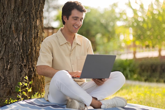 Sorridente freelance uomo millenario che lavora al parco pubblico