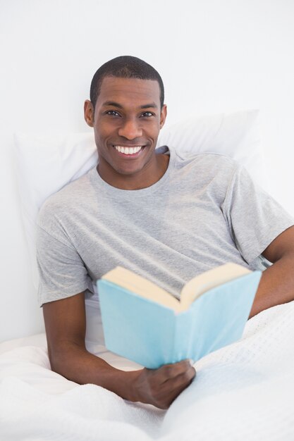 Sorridente giovane afro con un libro a letto