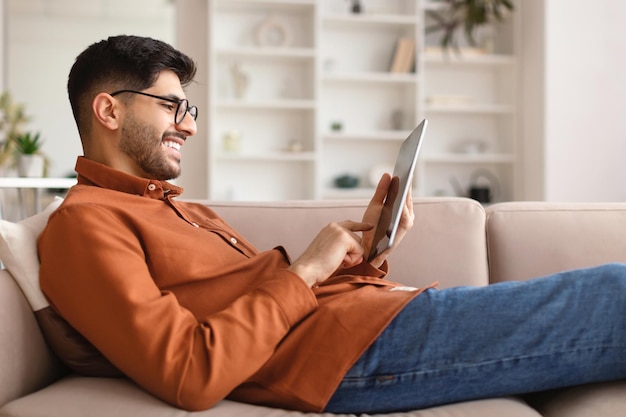 Sorridente giovane arabo utilizzando tavoletta digitale a casa