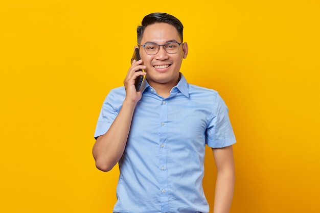 Sorridente giovane asiatico asiatico con gli occhiali parlando al cellulare isolato su sfondo giallo concetto di uomo d'affari e imprenditore