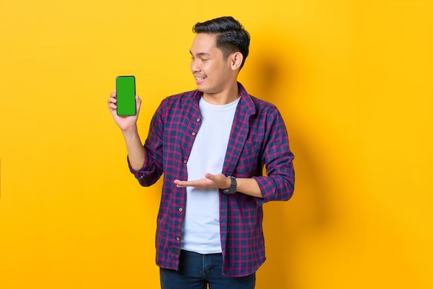 Sorridente giovane asiatico in camicia a quadri che mostra lo smartphone a schermo vuoto isolato su sfondo giallo