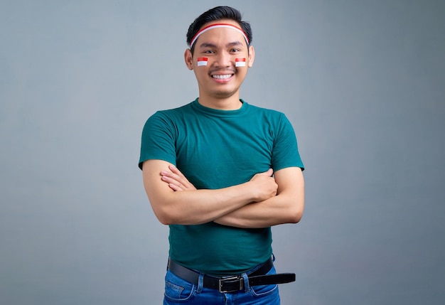 Sorridente giovane asiatico in maglietta casual in piedi con le braccia incrociate guardando la fotocamera isolata su sfondo grigio concetto di celebrazione del giorno dell'indipendenza dell'indonesia