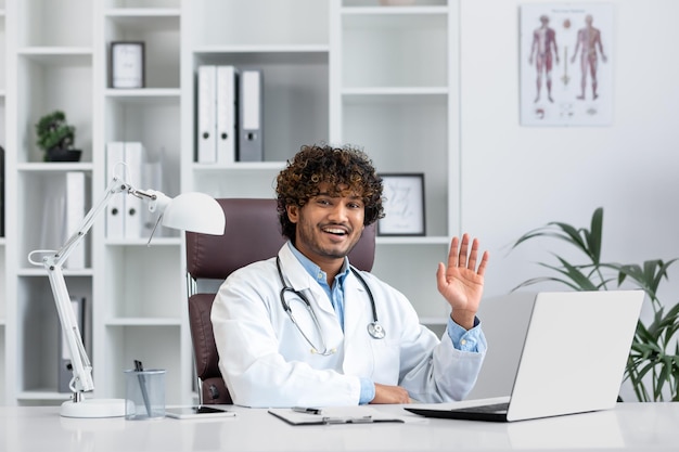 Sorridente giovane assistente stagista maschio ispanico medico studente seduto in ufficio a studiare computer portatile