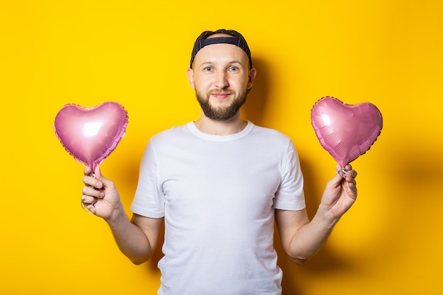 Sorridente giovane barbuto che tiene gli aerostati di aria cuore rosa