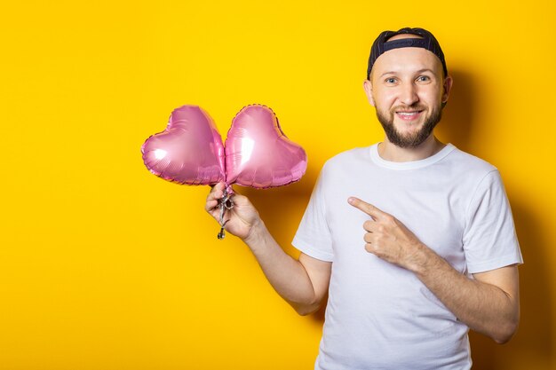 Sorridente giovane barbuto punta il dito contro i palloncini rosa aria