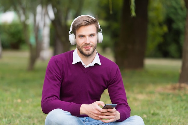 Sorridente giovane bel ragazzo che ascolta musica nel parco, tecnologia nella vita moderna.