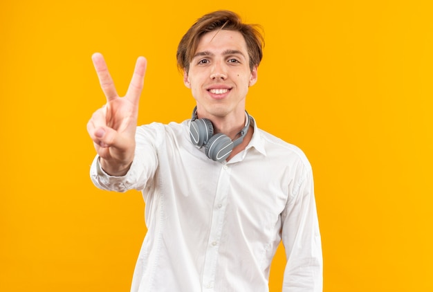 Sorridente giovane bel ragazzo che indossa una camicia bianca con le cuffie sul collo che mostra il gesto di pace