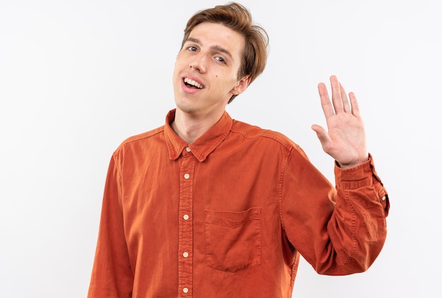 Sorridente giovane bel ragazzo che indossa una camicia rossa che mostra gesto di saluto isolato sul muro bianco