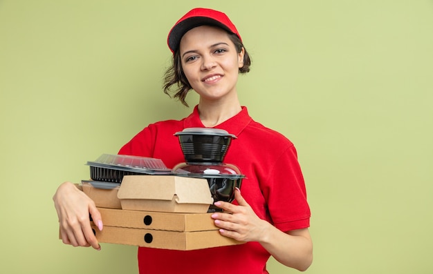 Sorridente giovane bella donna di consegna che tiene contenitori per alimenti e imballaggi su scatole per pizza