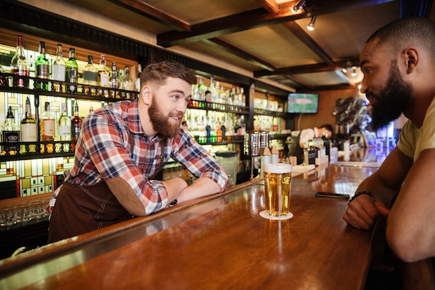 Sorridente giovane bere birra e parlare con il barista in pub