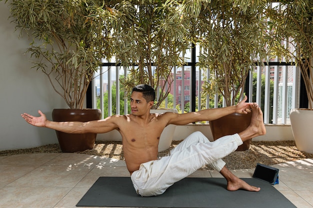 Sorridente giovane brasiliano prendendo lezioni di yoga online e tenendo il suo alluce.