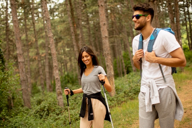 Sorridente giovane coppia che cammina con gli zaini nella foresta in una giornata estiva