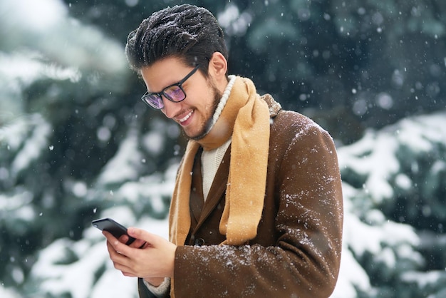 Sorridente giovane divertirsi all'aperto. L'uomo d'affari usa un telefono. concetto di inverno. Nevicata.