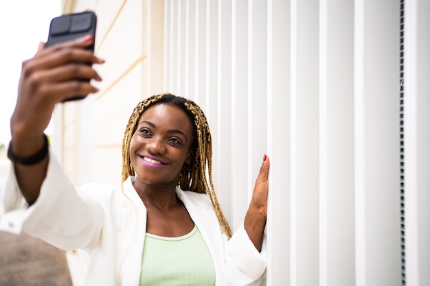 Sorridente giovane donna africana adulta che prende selfie con un cellulare all'aperto