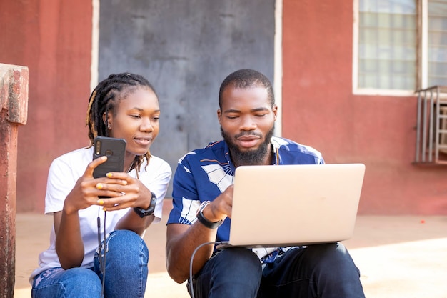 Sorridente giovane donna africana e uomo che guarda lo schermo del laptop controllando le finanze navigando online lavora femmina tenendo il telefono cellulare