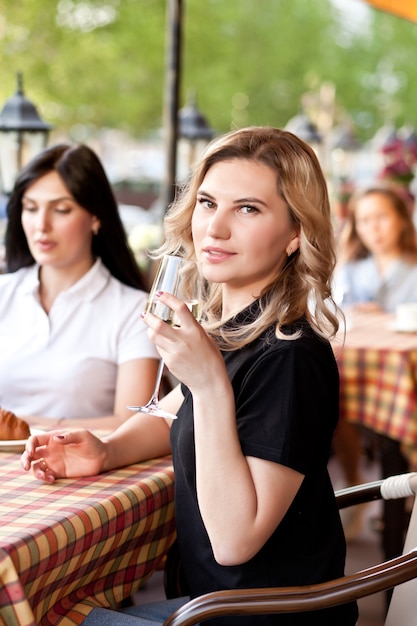 Sorridente giovane donna al caffè a bere vino bianco. Comunicazione e concetto di amicizia.