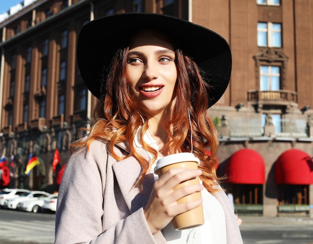 Sorridente giovane donna alla moda che beve caffè mentre si cammina su una strada cittadina