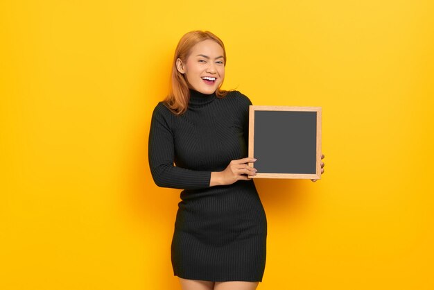 Sorridente giovane donna asiatica che tiene lavagna isolata su sfondo giallo