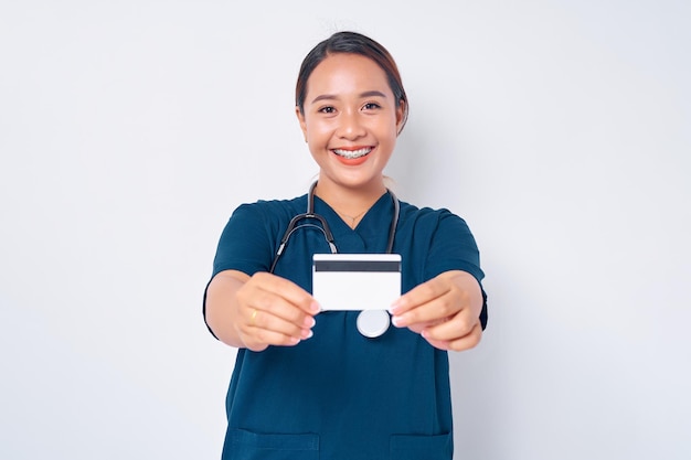 Sorridente giovane donna asiatica infermiera professionale che lavora indossando uniforme blu tenendo la carta di credito bancaria isolata su sfondo bianco Concetto di medicina sanitaria