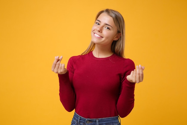 Sorridente giovane donna bionda ragazza in abbigliamento casual in posa isolato su sfondo giallo arancione muro. Concetto di stile di vita delle persone. Simula lo spazio della copia. Strofinare le dita mostrando un gesto in contanti che chiede soldi.