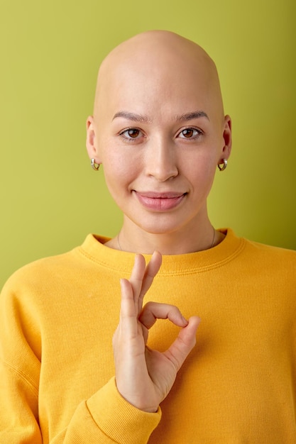 Sorridente giovane donna calva che indossa una camicia gialla in posa isolata su sfondo verde