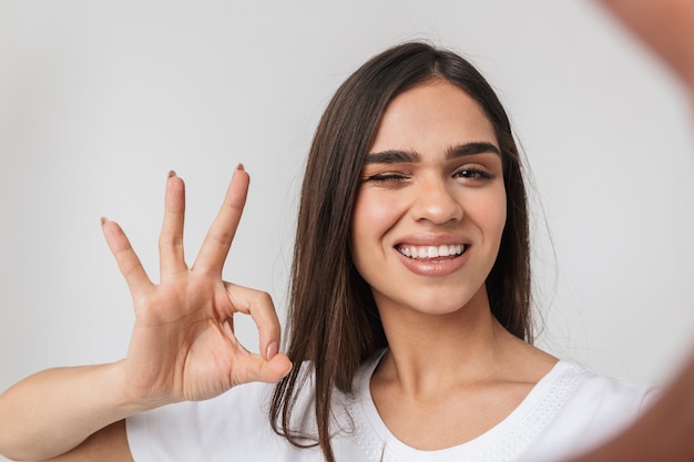 Sorridente giovane donna casualy vestito in piedi isolato su bianco, prendendo un selfie con le mani estese