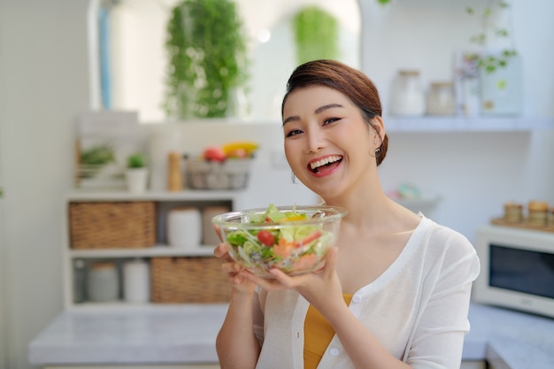 Sorridente giovane donna che mangia insalata fresca in cucina moderna