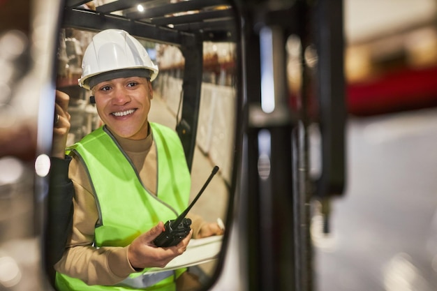 Sorridente giovane donna che opera carrello elevatore in magazzino
